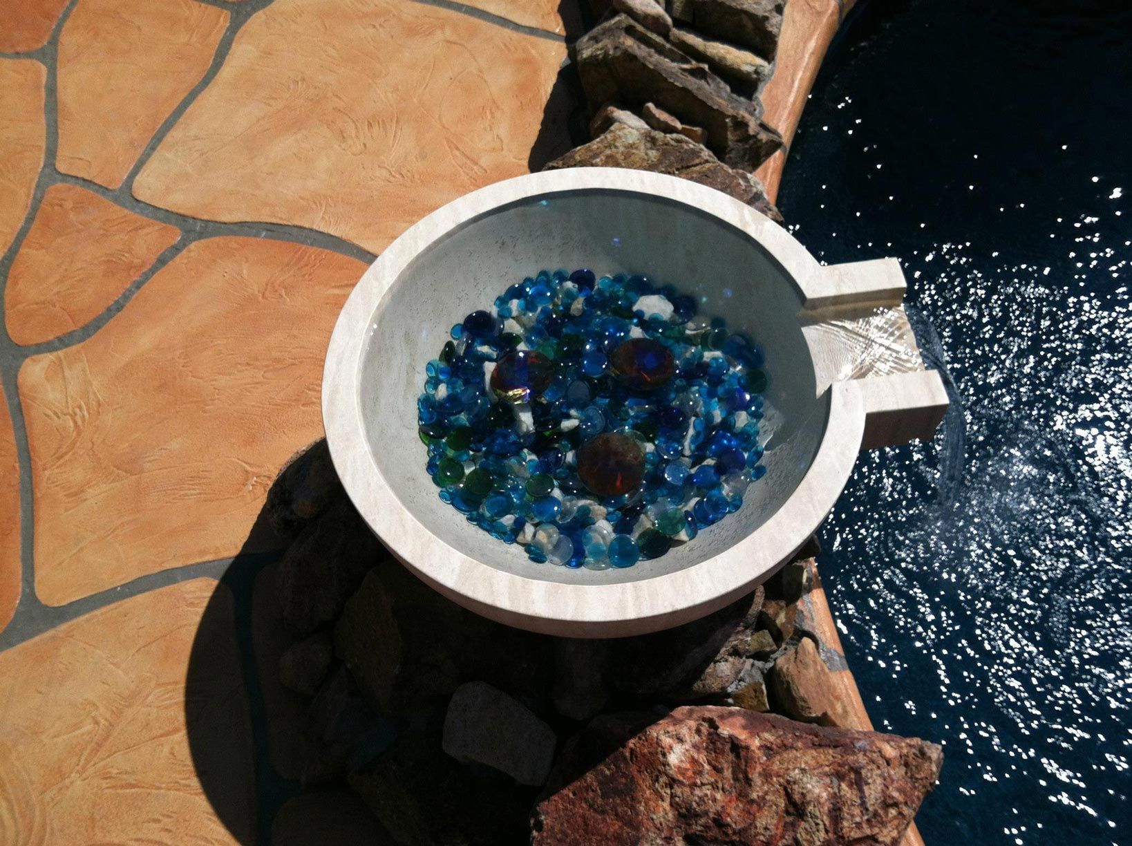 A bowl filled with blue glass beads sits next to a pool