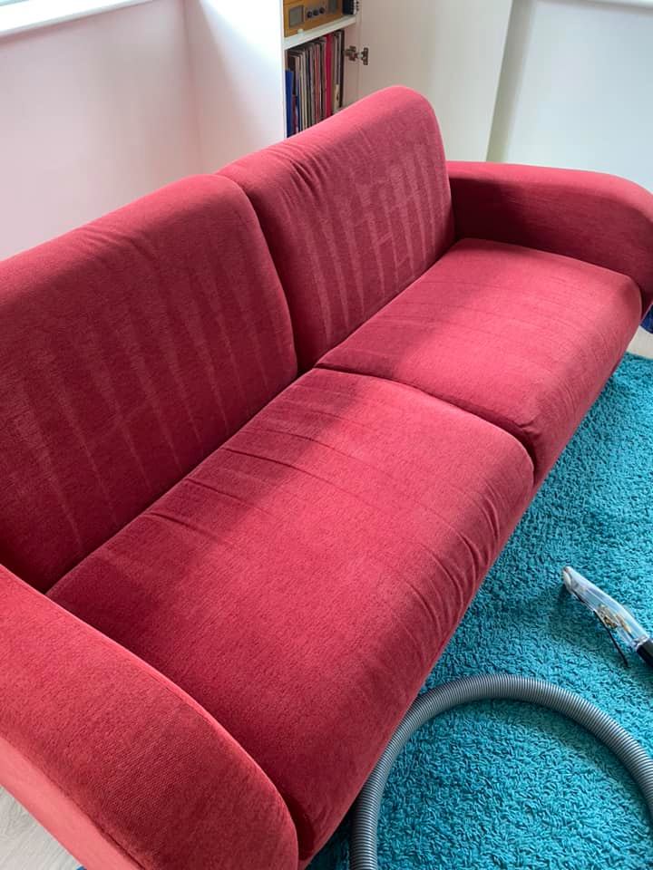 a red couch is sitting on a blue rug next to a vacuum cleaner .