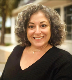 A woman with curly hair wearing a black shirt smiles for the camera