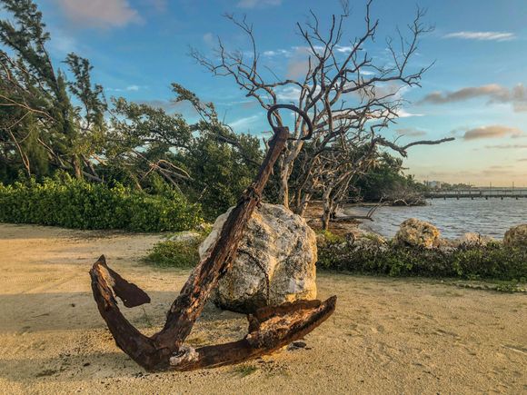 An old rusty anchor is sitting on top of a large rock on the beach.