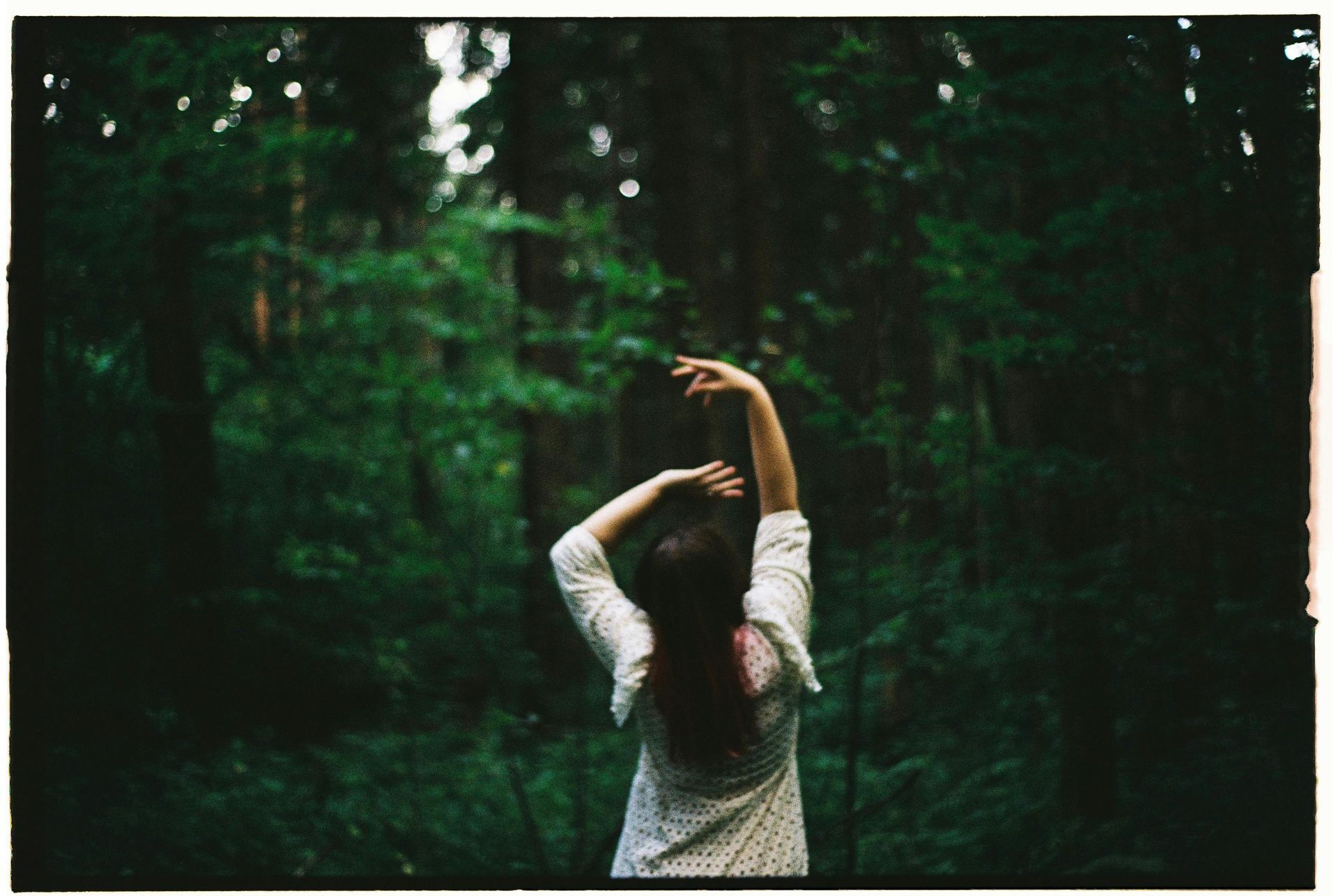 Woman in forrest with arms over her head.