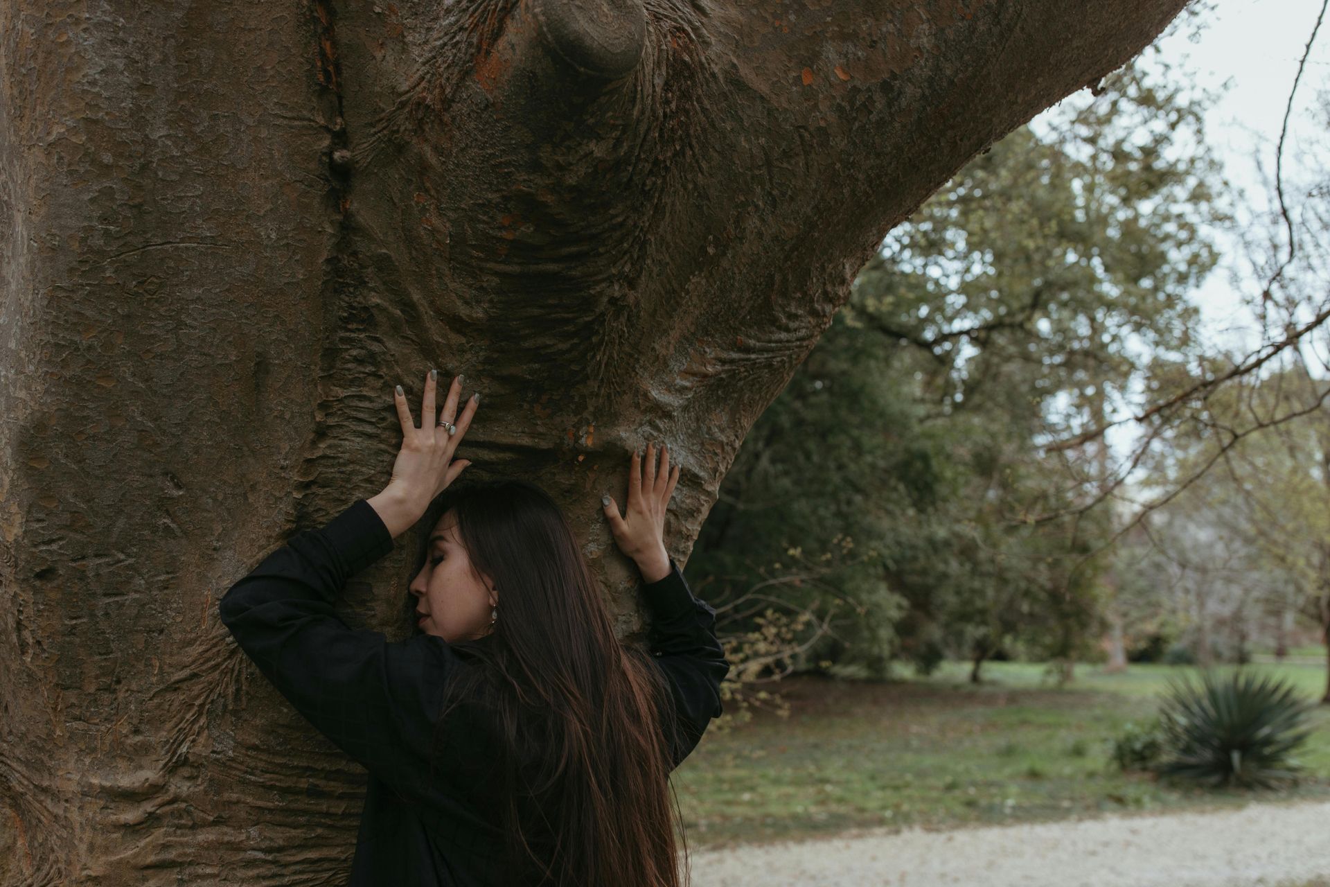 What is a somatic therapist? Woman leaning against a tree with her hands splayed on it over her head