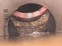 Inside of a pipe, possibly sewer. Dark, murky water, brown and tan debris. Top has pinkish color.