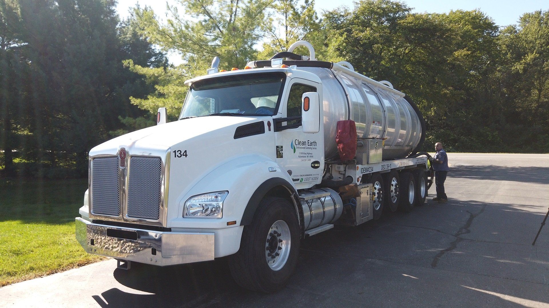 White tanker truck on asphalt road next to grass and trees.
