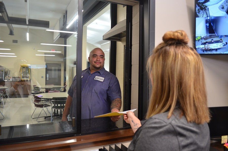 Man at a window smiles, handing a paper to a woman. Office setting, neutral tones.