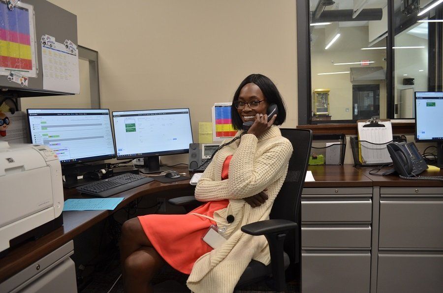 Woman in office at desk, on the phone, wearing orange dress and cream cardigan.