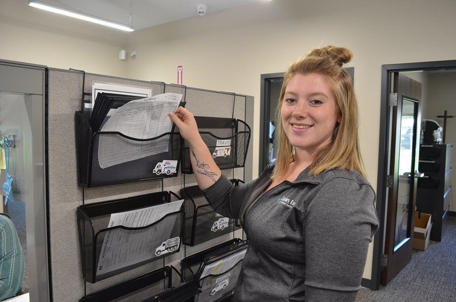 Woman in gray top, smiling, reaching for paper in a wall-mounted organizer in an office.