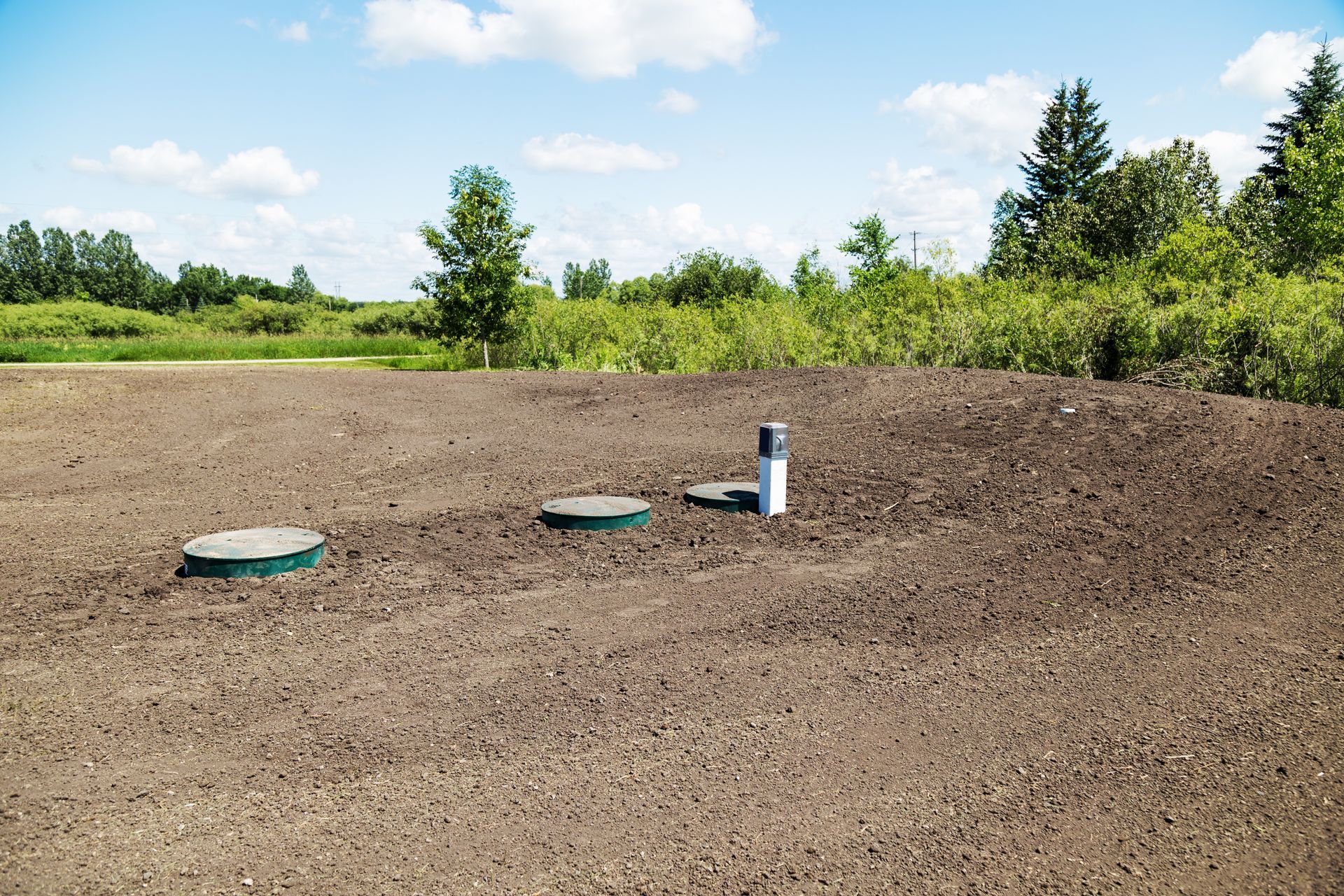Septic system covers and vent pipe installed on soil mound in rural outdoor setting.