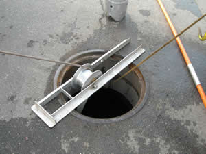Manhole with tool inserted, pulling wire. Metal frame rests across the opening.