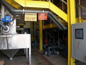 Industrial interior with yellow beams, pipes, signs, and control panel.