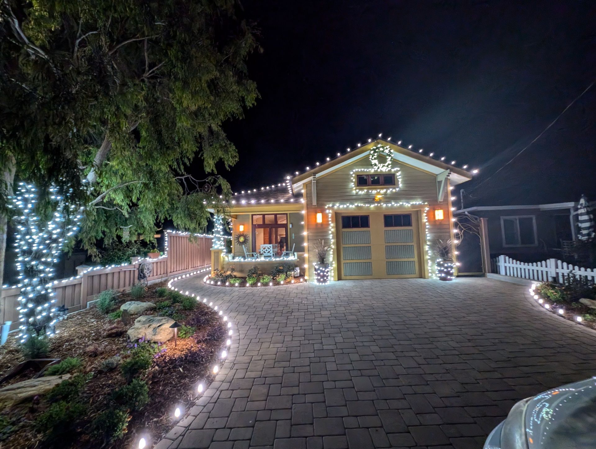 A house is decorated with christmas lights and a white picket fence