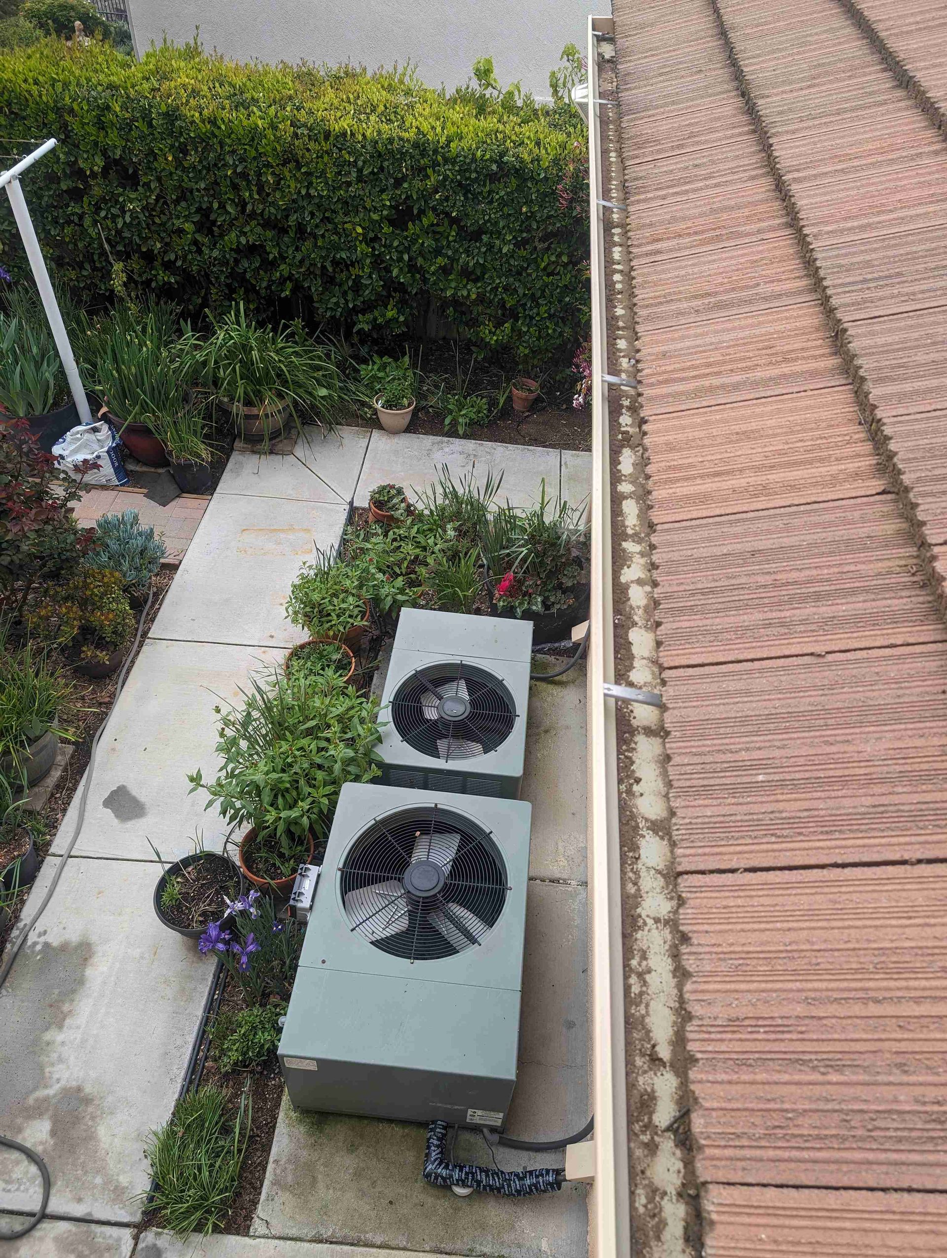 Two air conditioners are sitting on the sidewalk next to a gutter.
