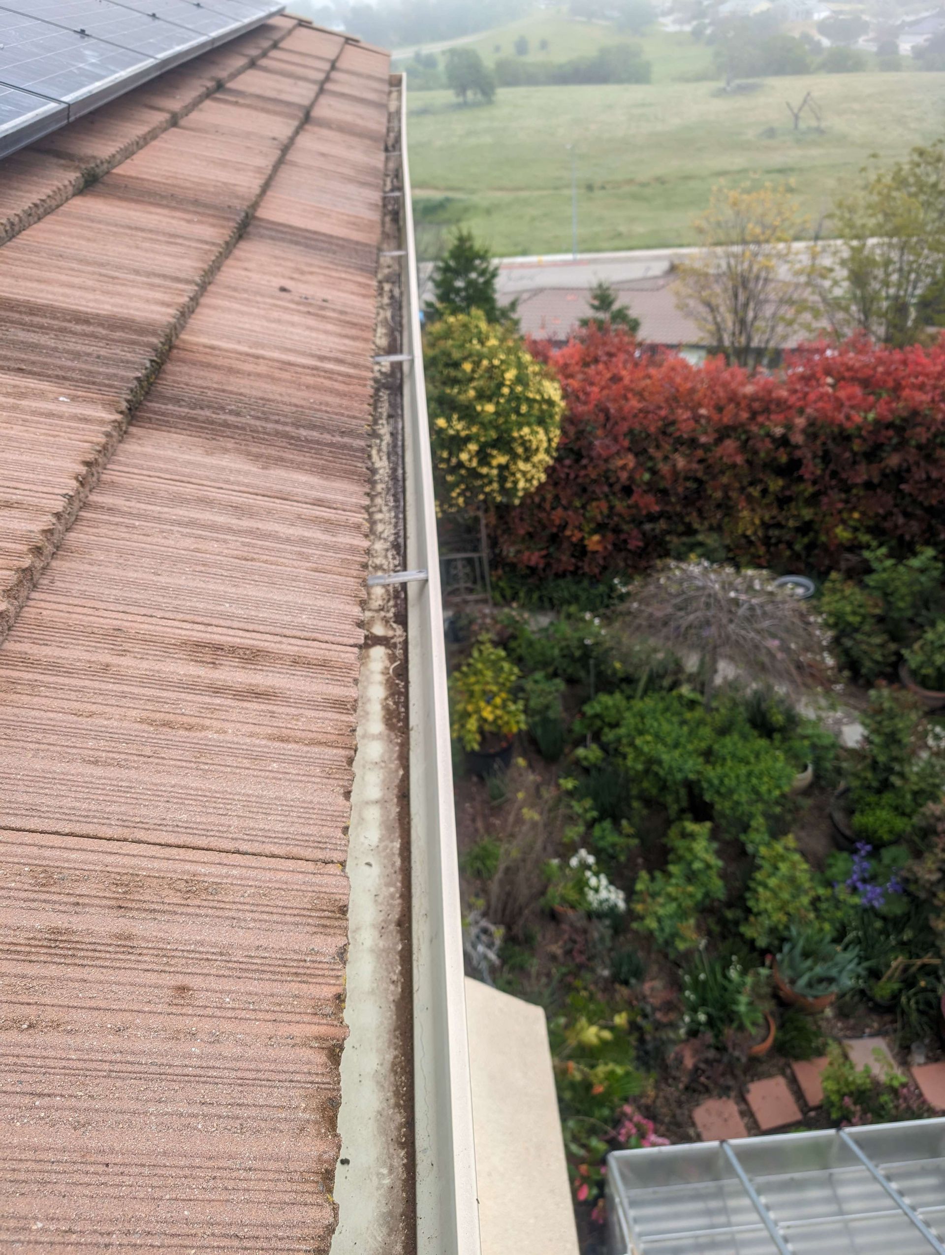 Roof with a gutter on it and a garden in the background