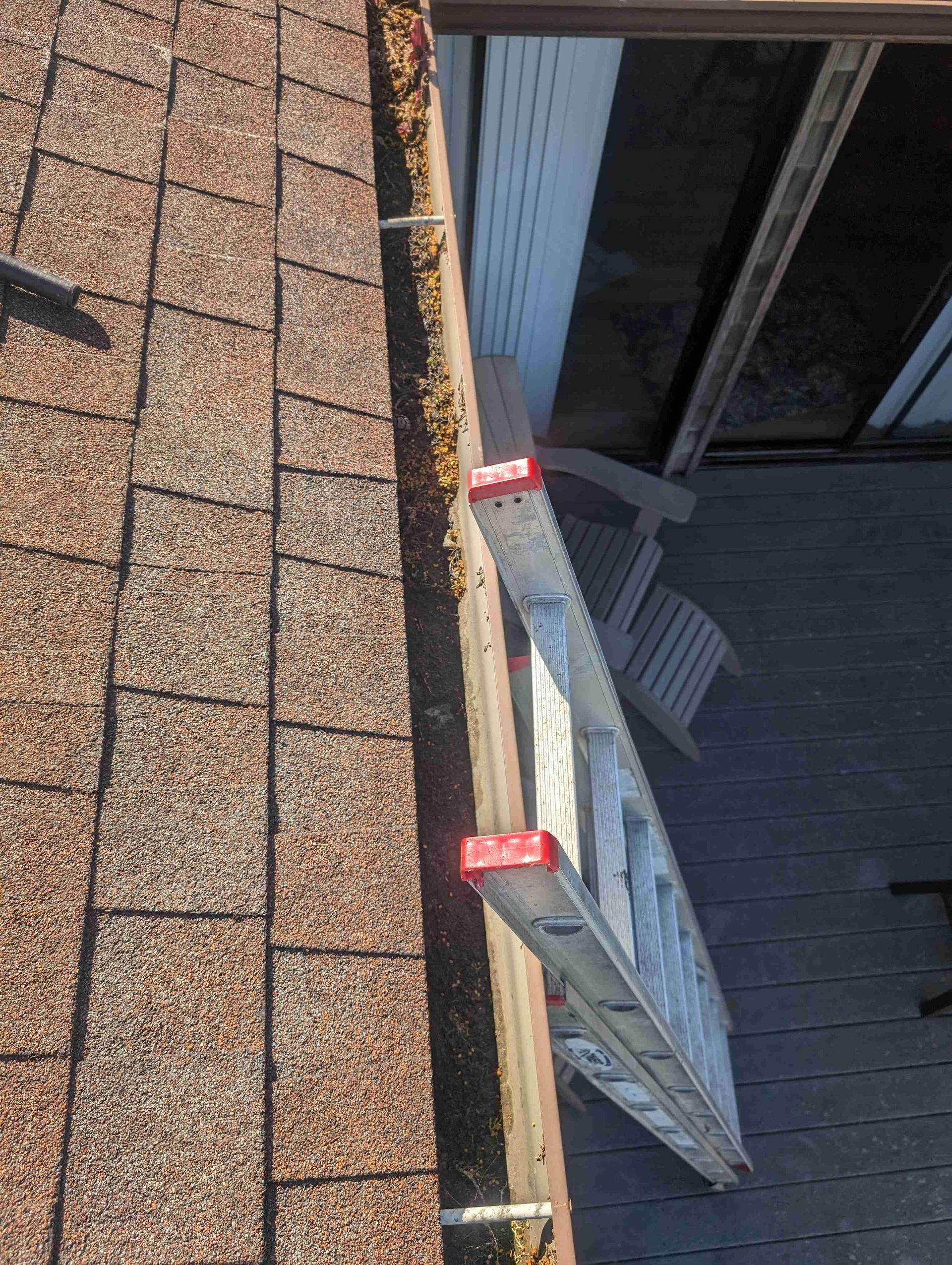 Ladder is sitting on top of a gutter on a roof.