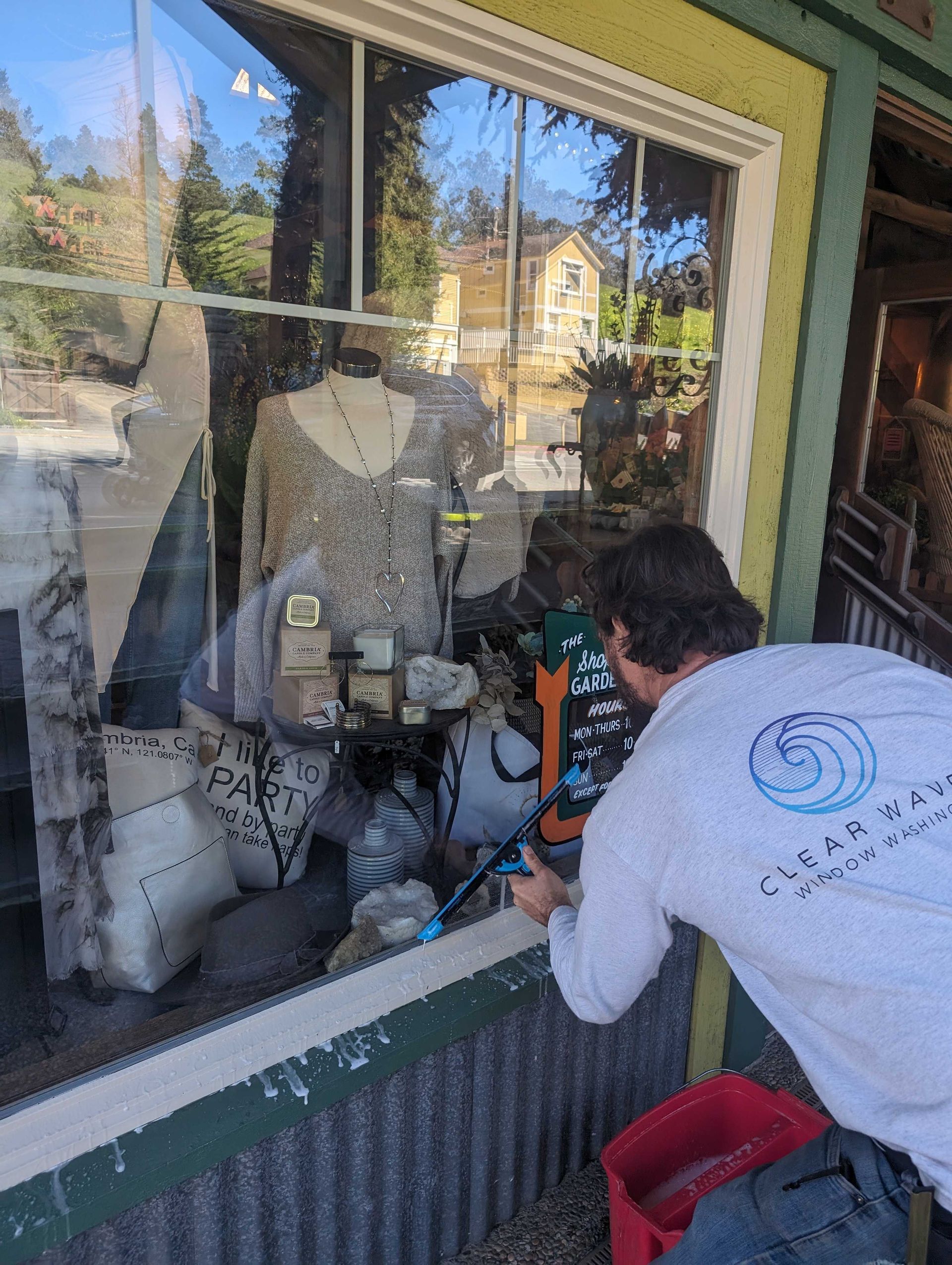 Man is cleaning a store window with a hose.