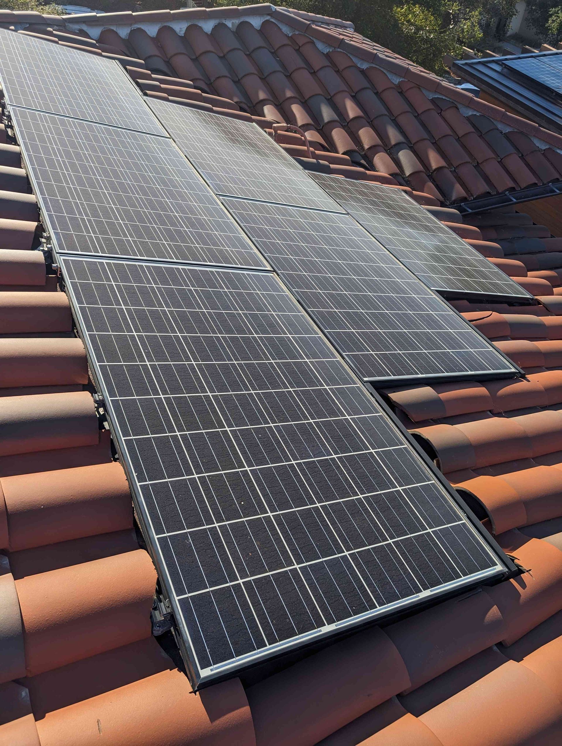 A row of solar panels are sitting on top of a tiled roof.