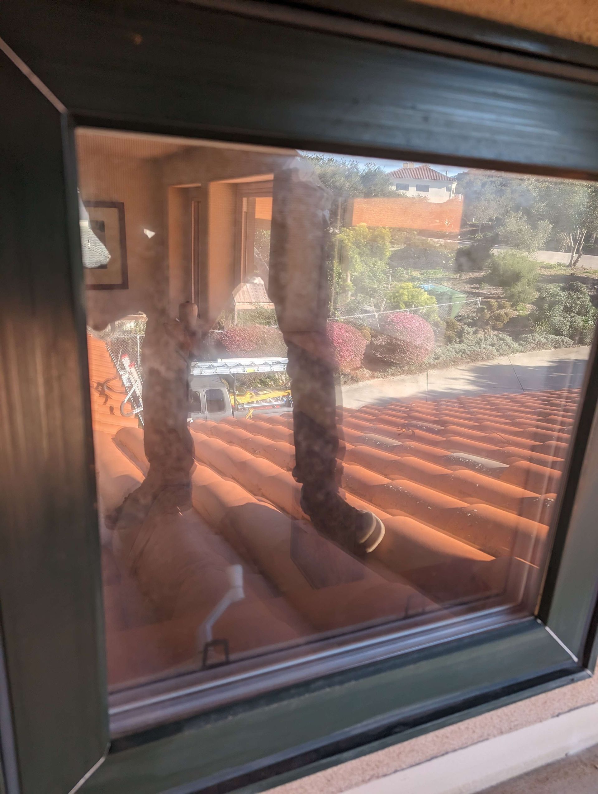 A person is standing on a roof looking out of a window.