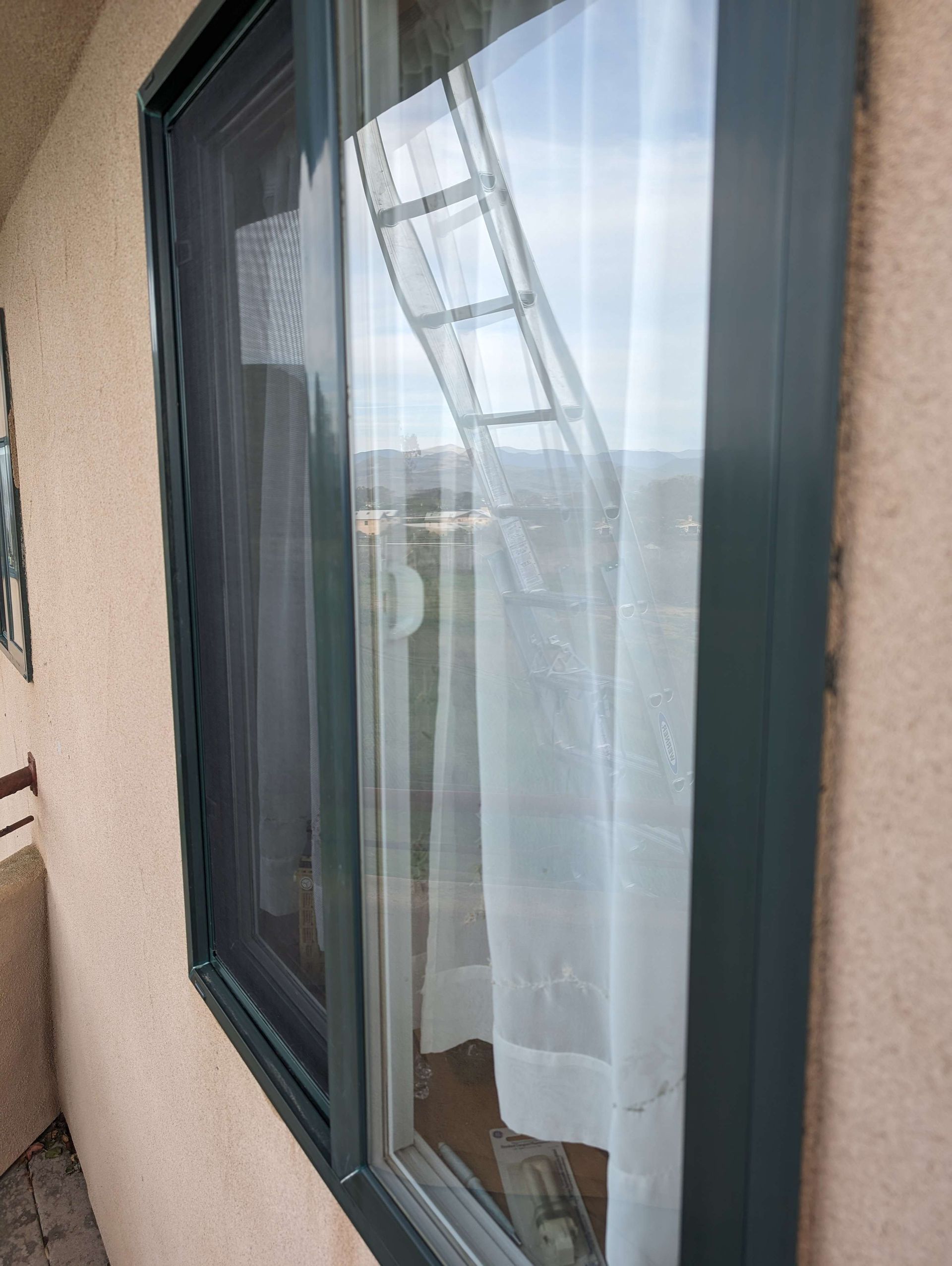 A window on the side of a building with a ladder reflected in it.