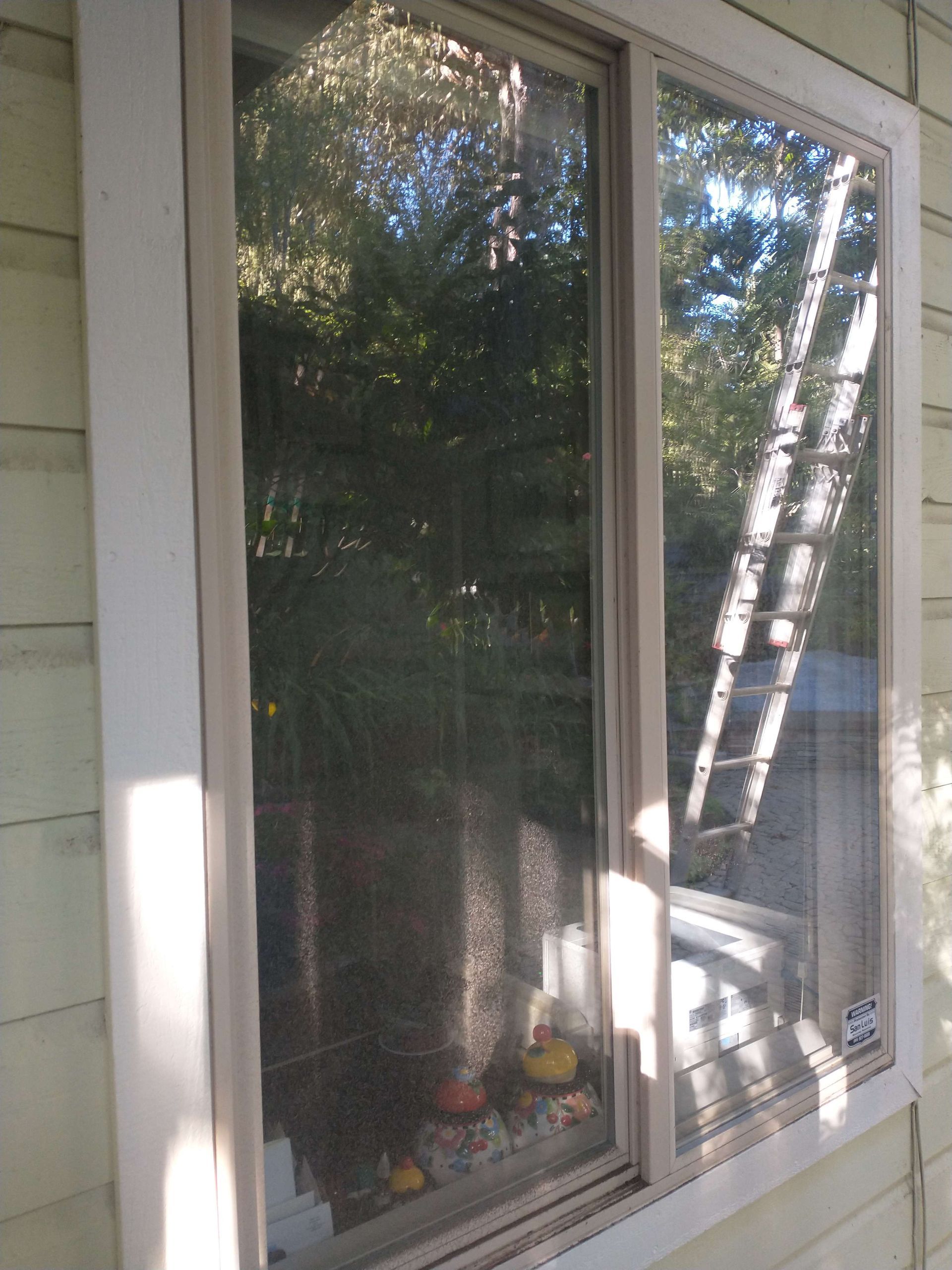 A window on the side of a house with a ladder in the background
