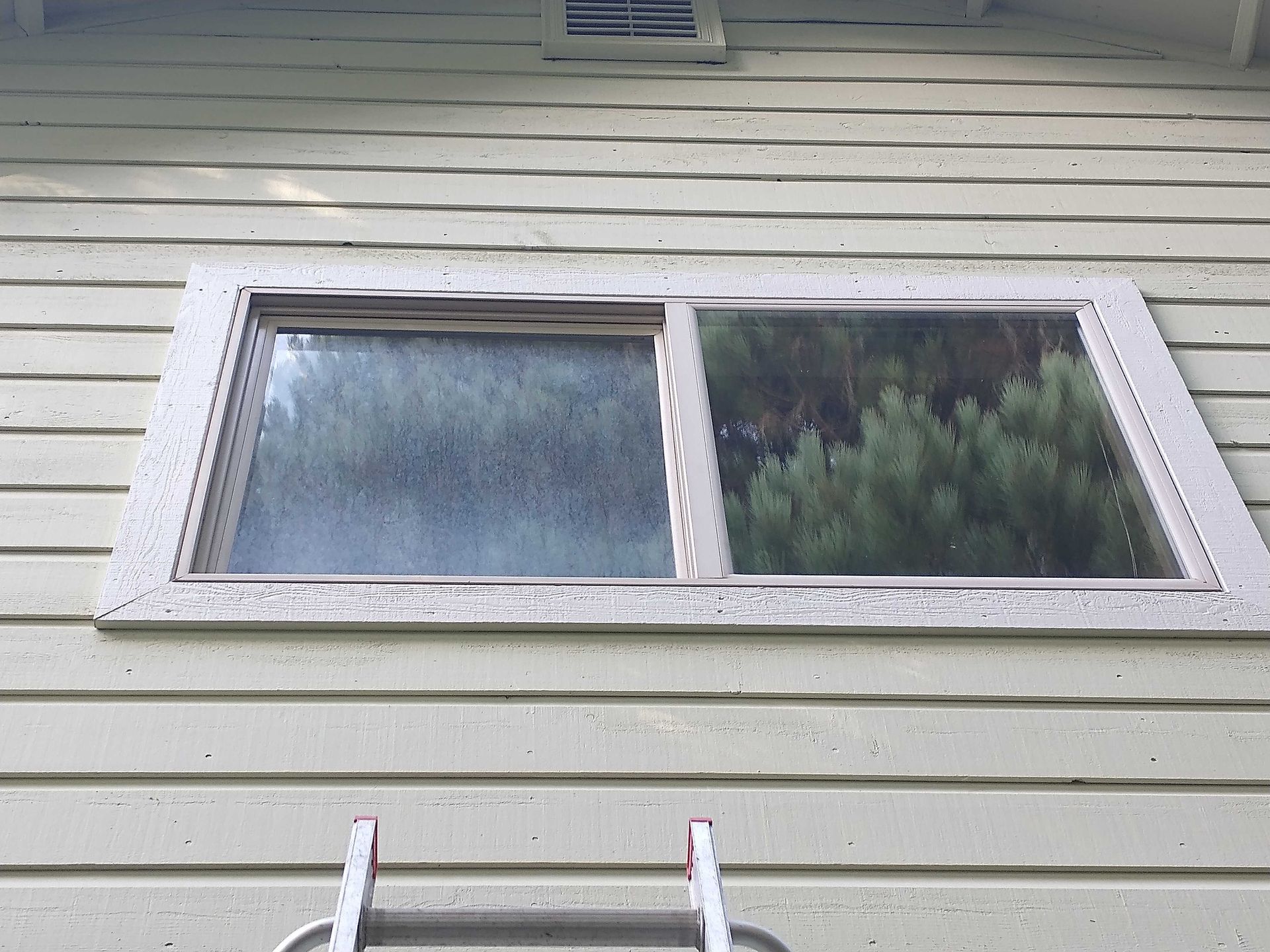 A window on the side of a house with a ladder next to it.