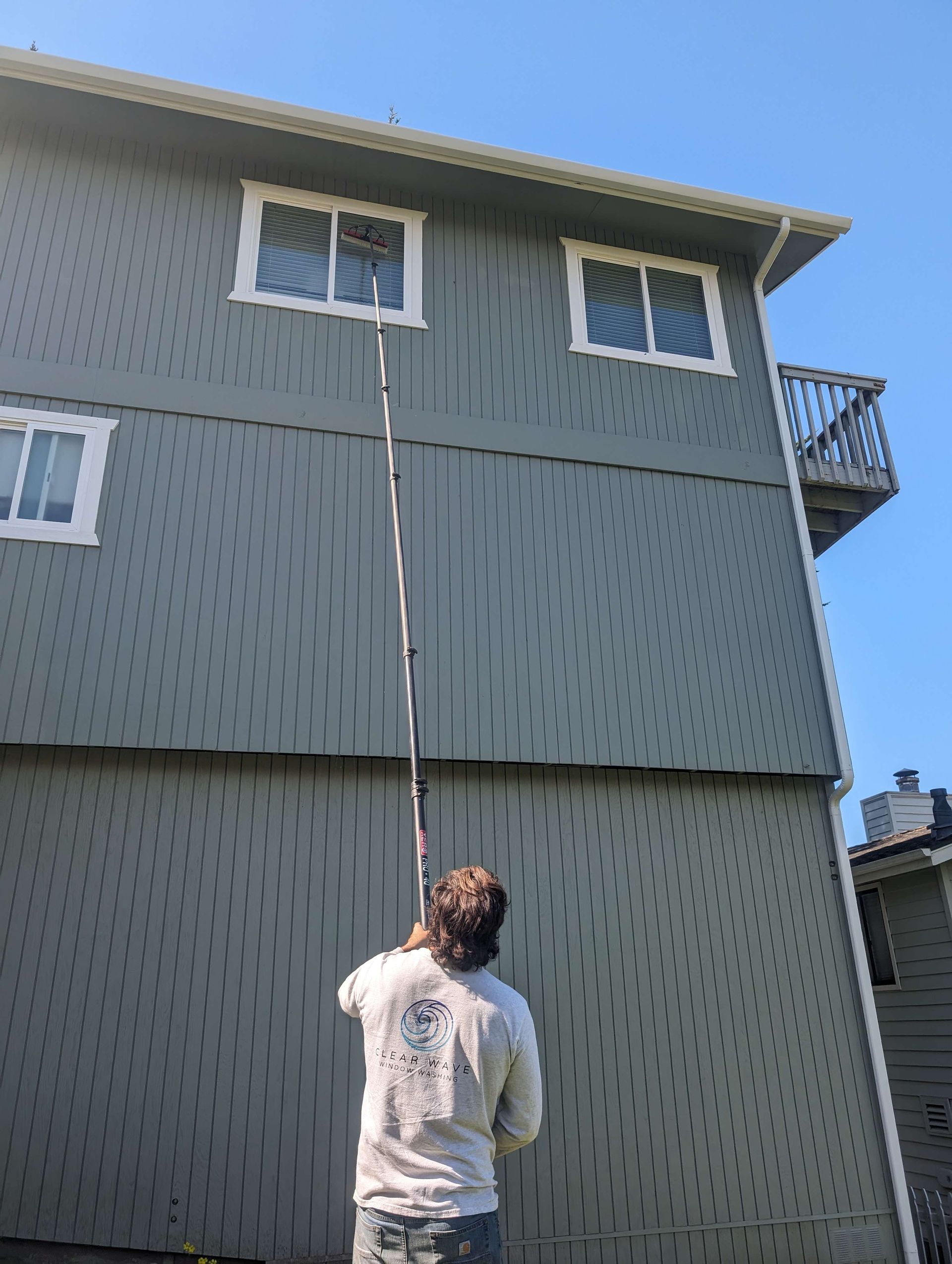 A man is cleaning the windows of a building with a long pole.