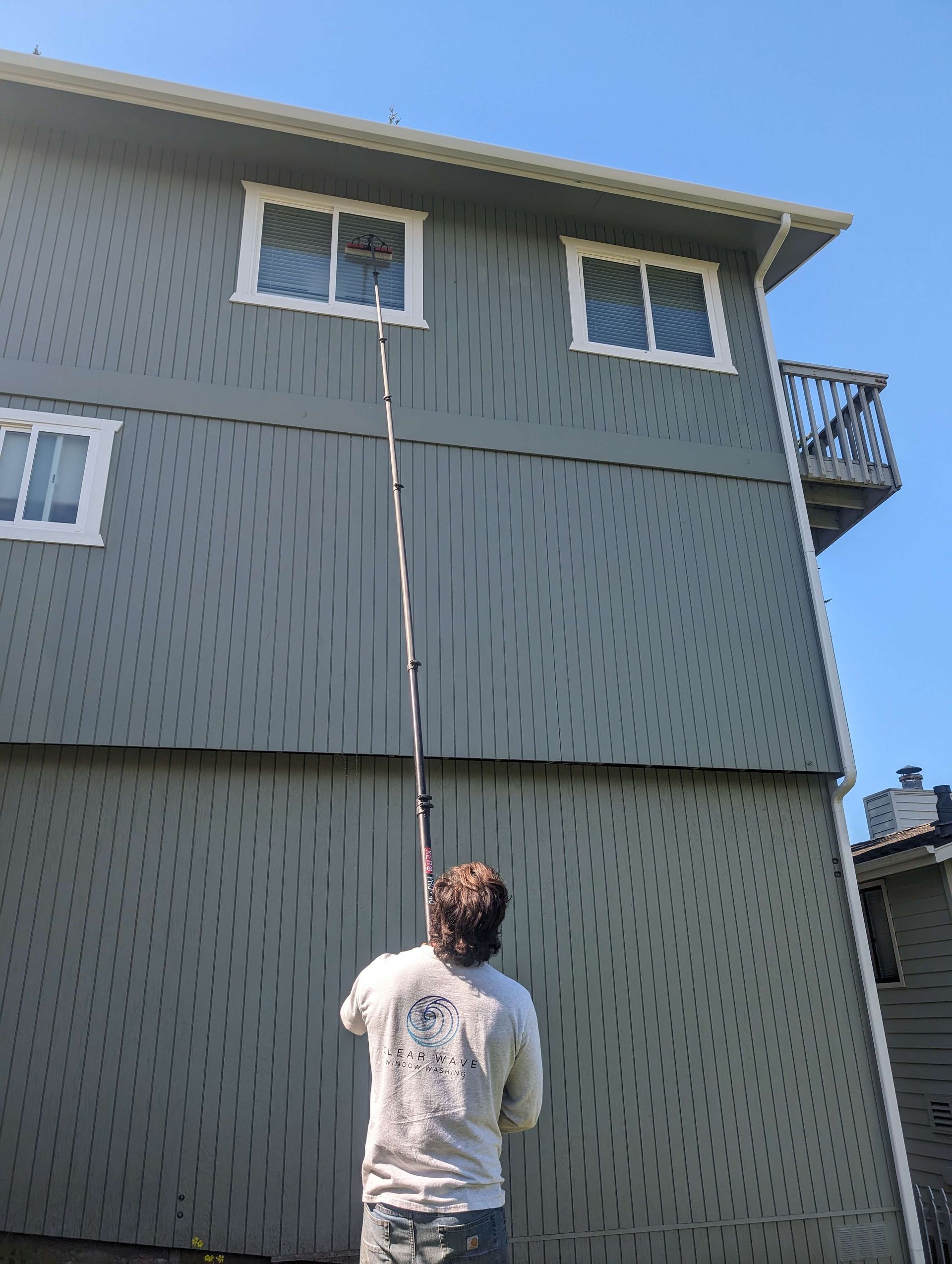 A man is cleaning the windows of a house with a long pole.