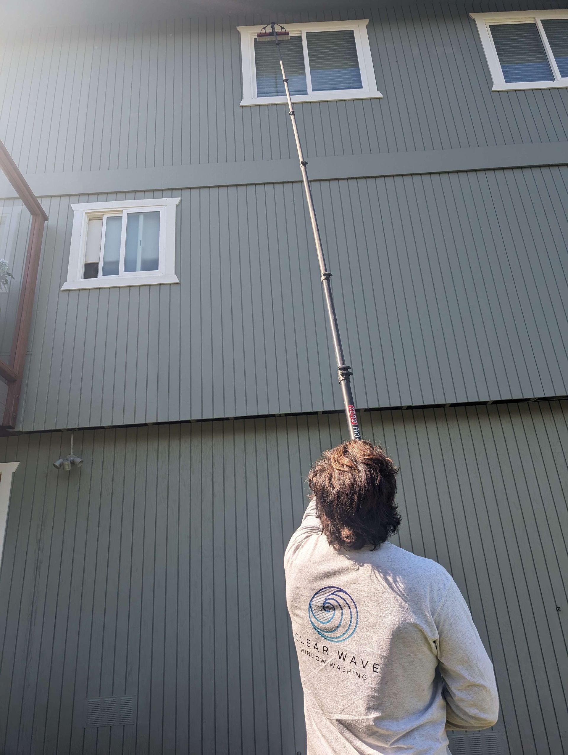A man is cleaning the windows of a building with a pole.