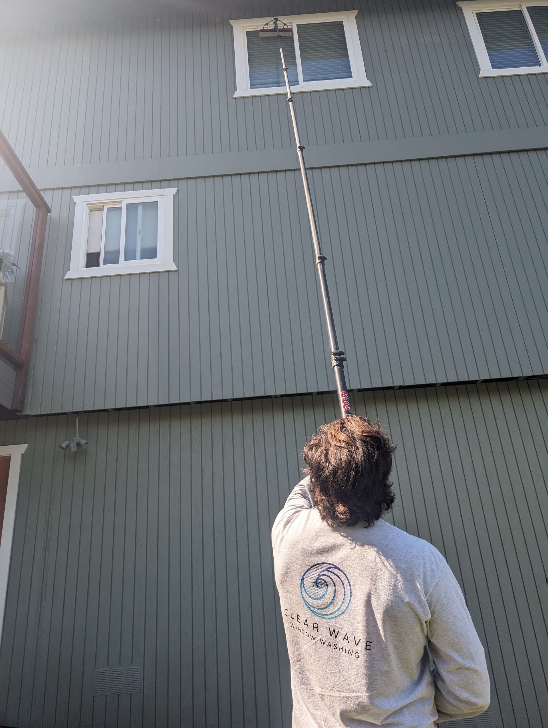 A man is cleaning the windows of a house with a long pole.