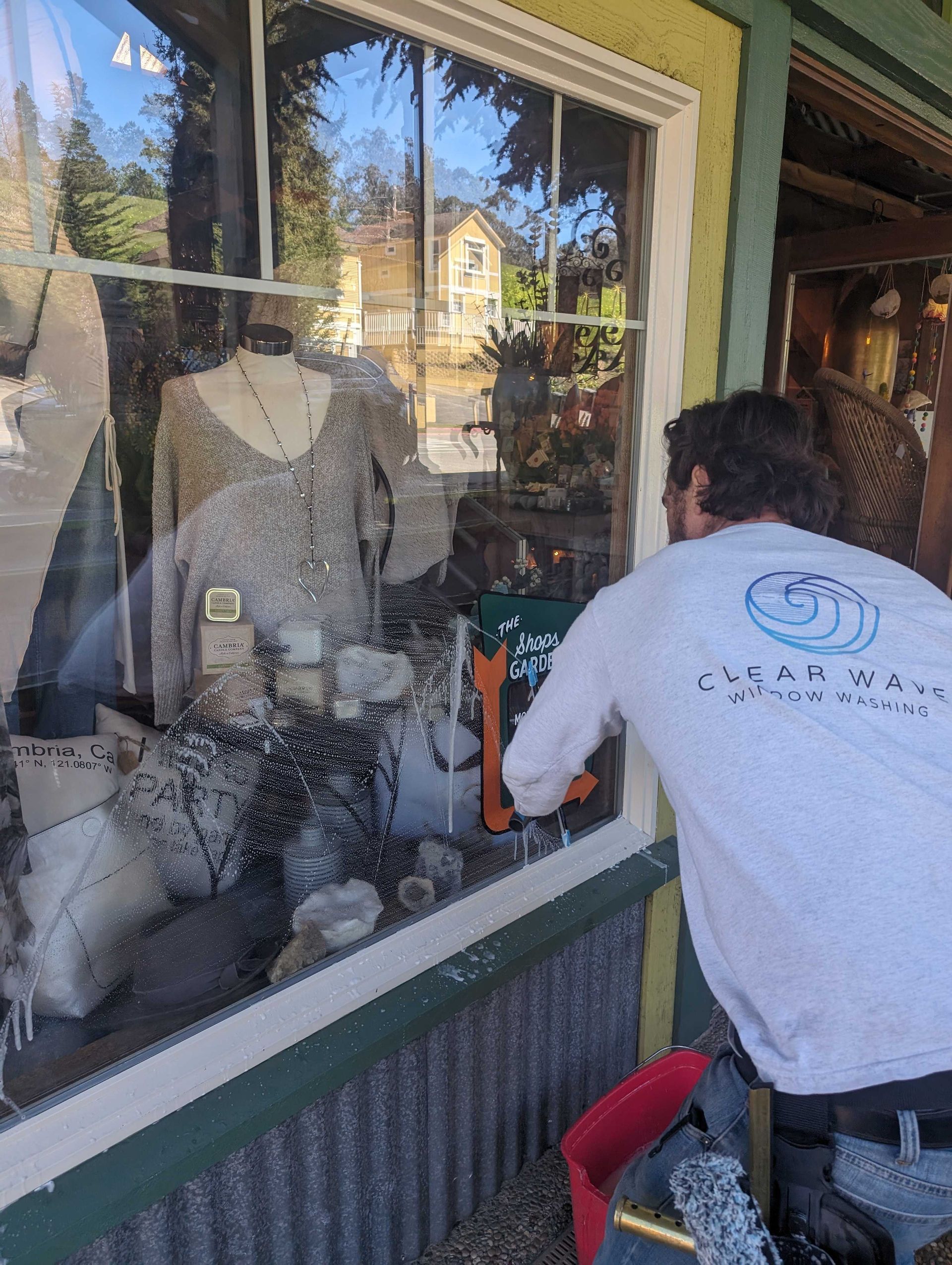 A man in a white shirt is cleaning a store window.