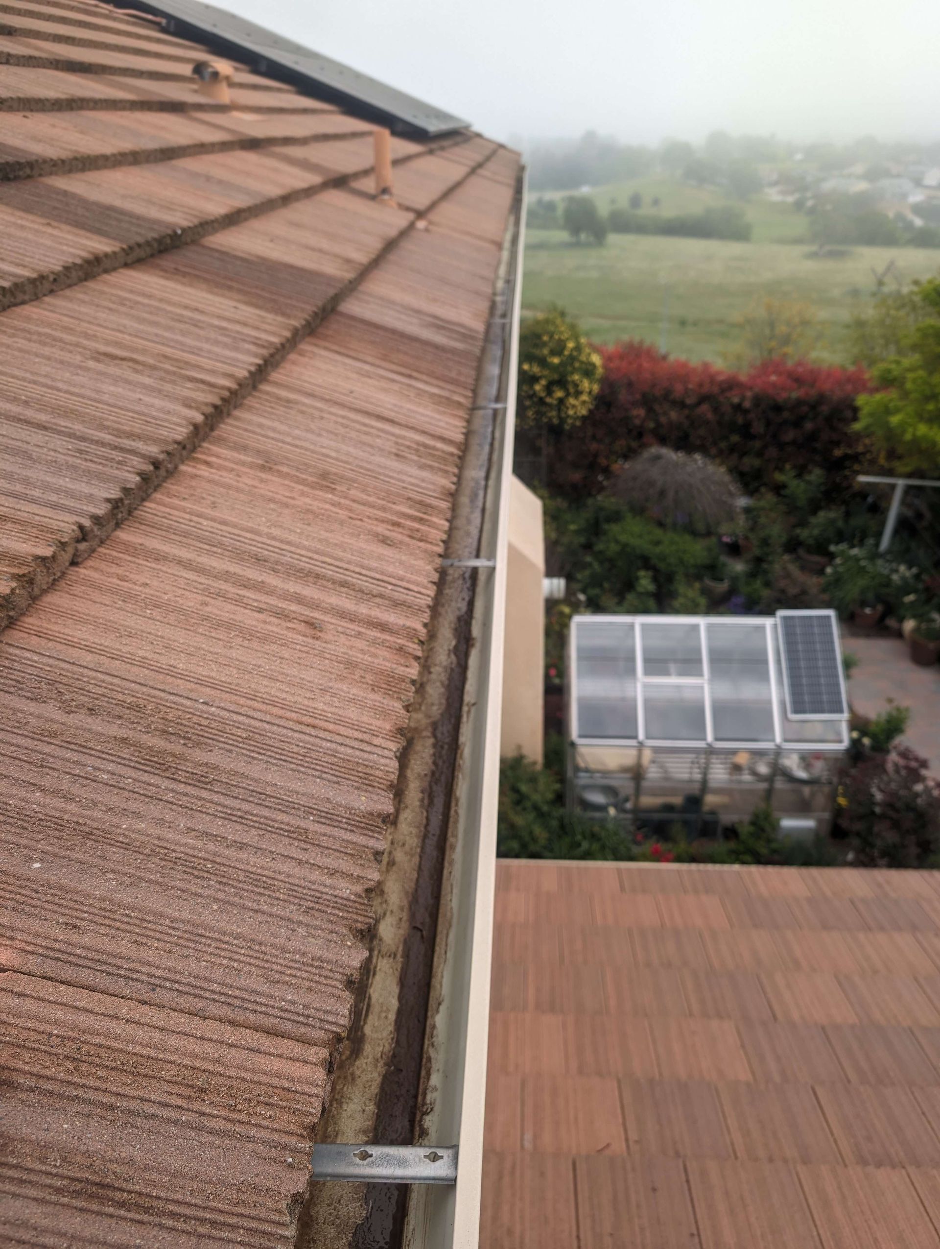 A roof with a gutter on it and a greenhouse in the background