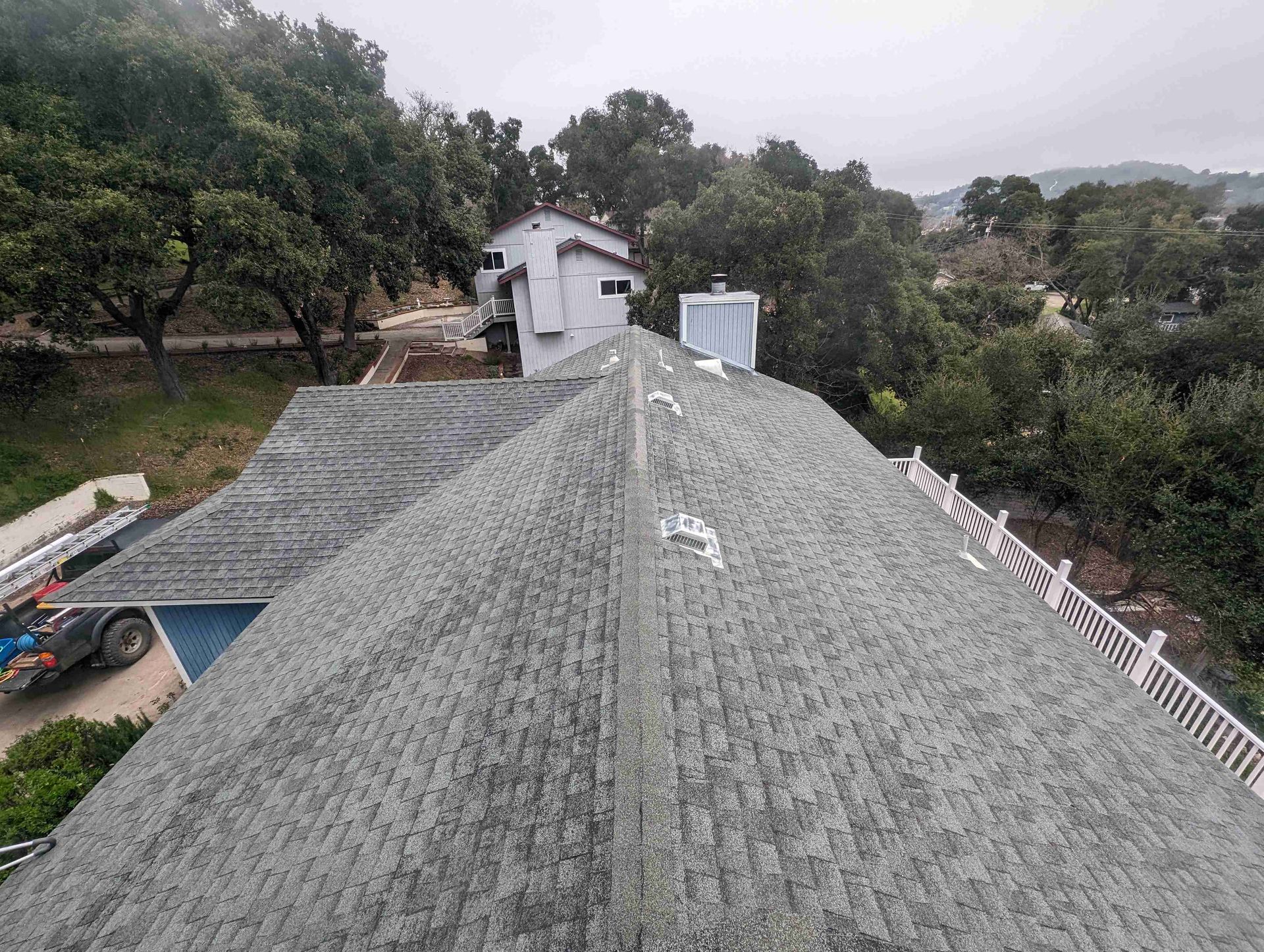 An aerial view of a roof of a house with a pool and trees in the background.