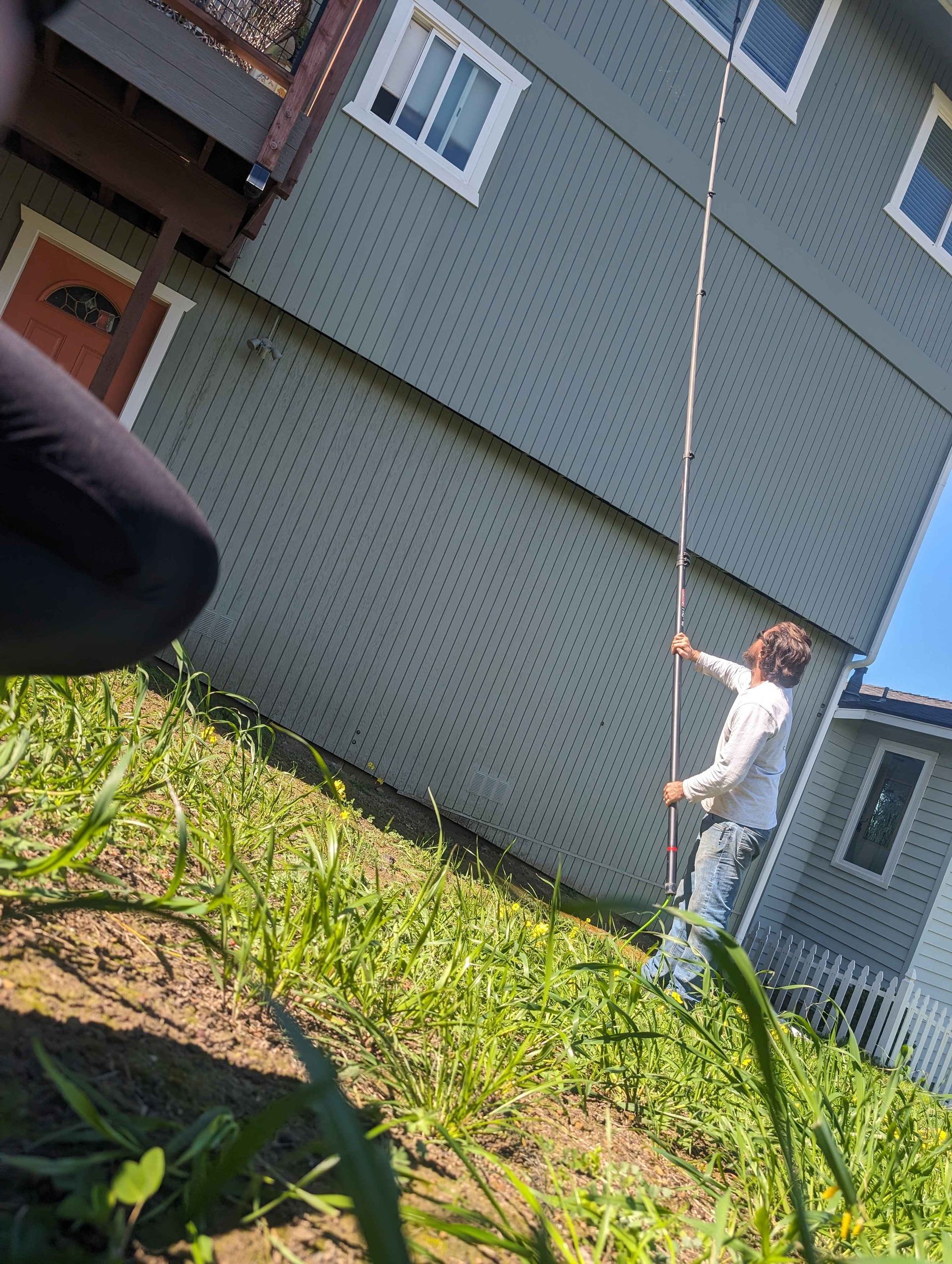 A man is standing in front of a house holding a pole.