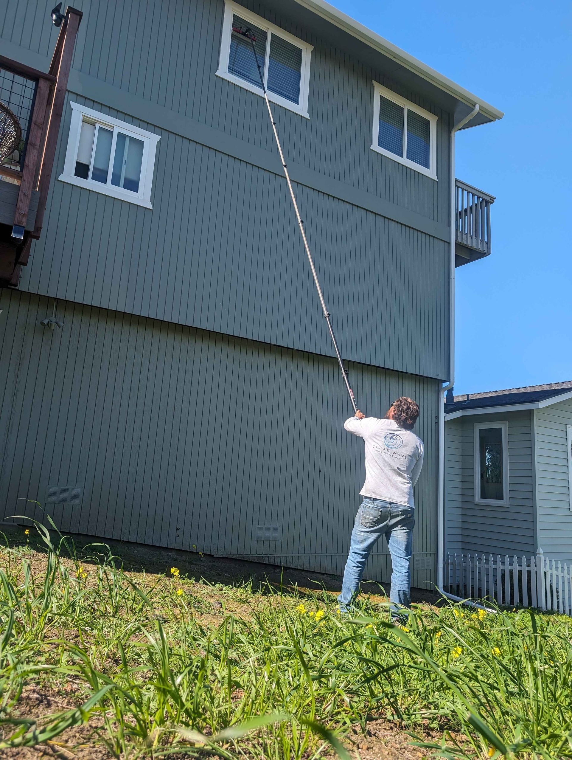 A man is cleaning the side of a house with a long pole.