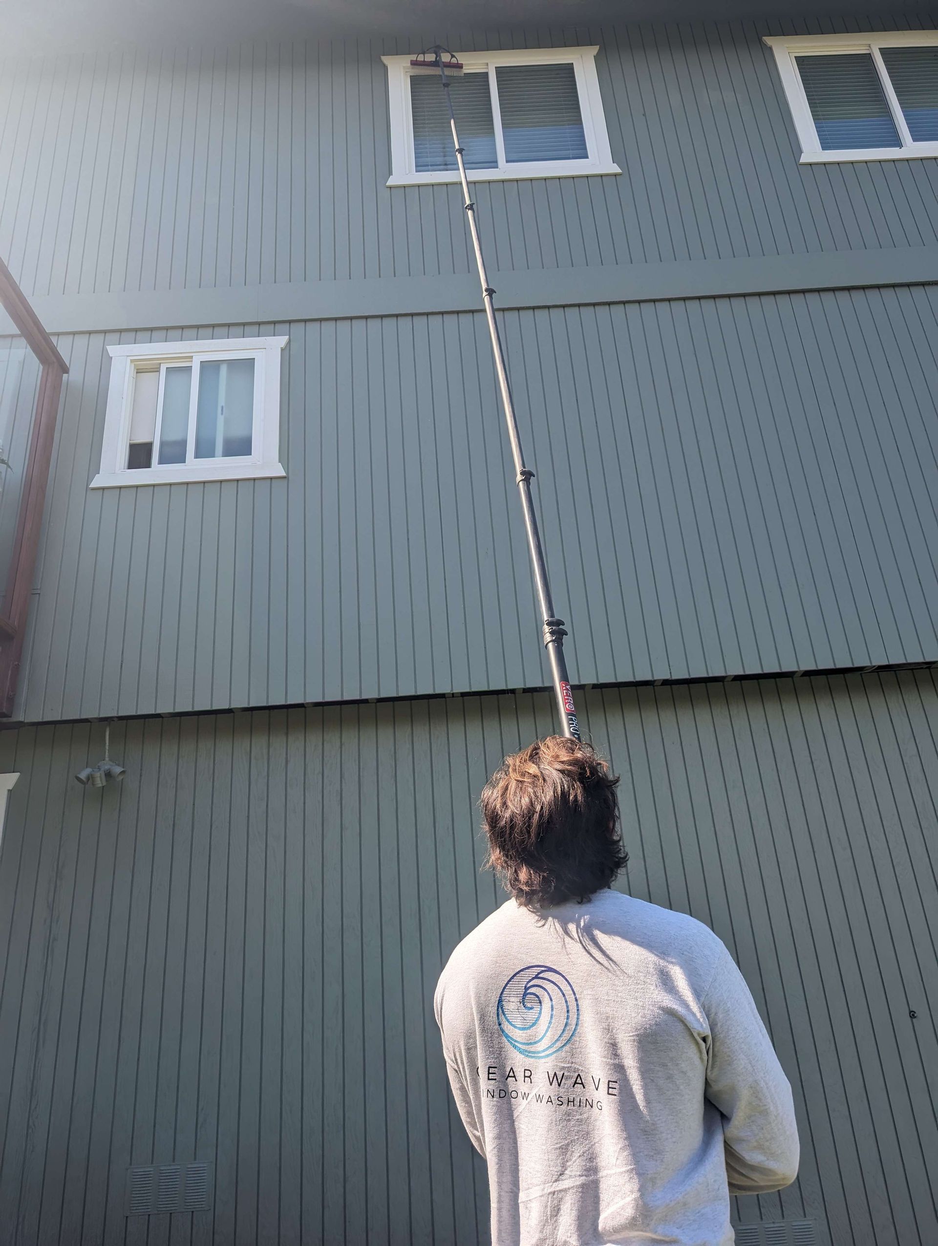 A man is cleaning the windows of a building with a long pole.