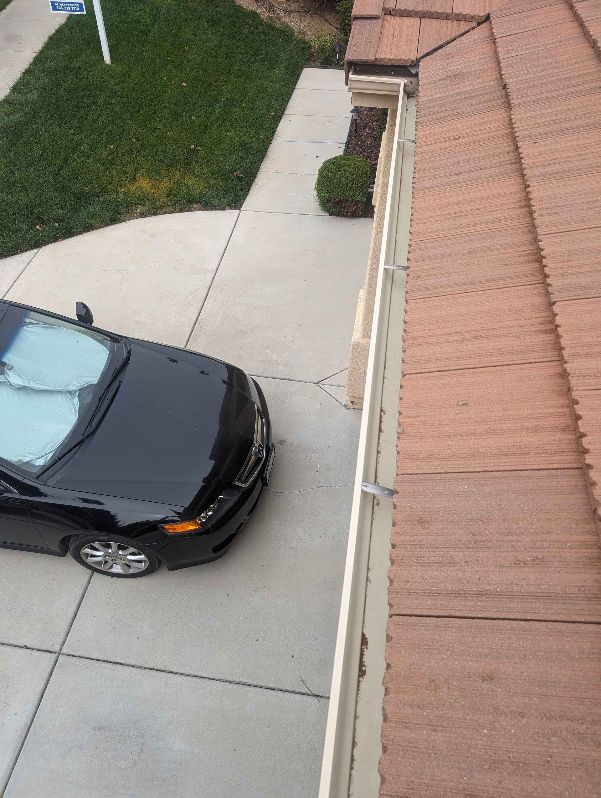 Black car is parked in a driveway next to a gutter.