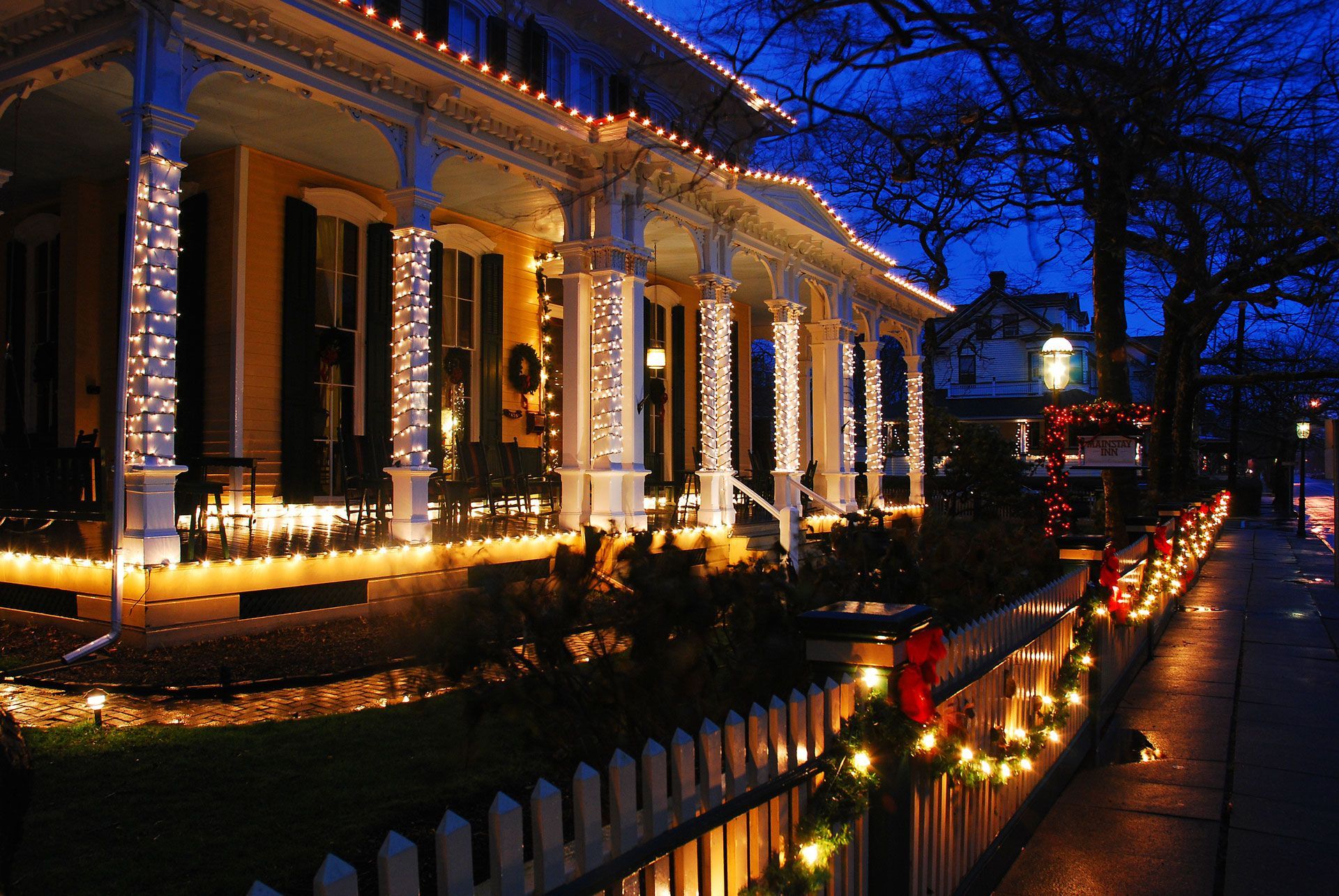 A house is decorated with christmas lights and a white picket fence