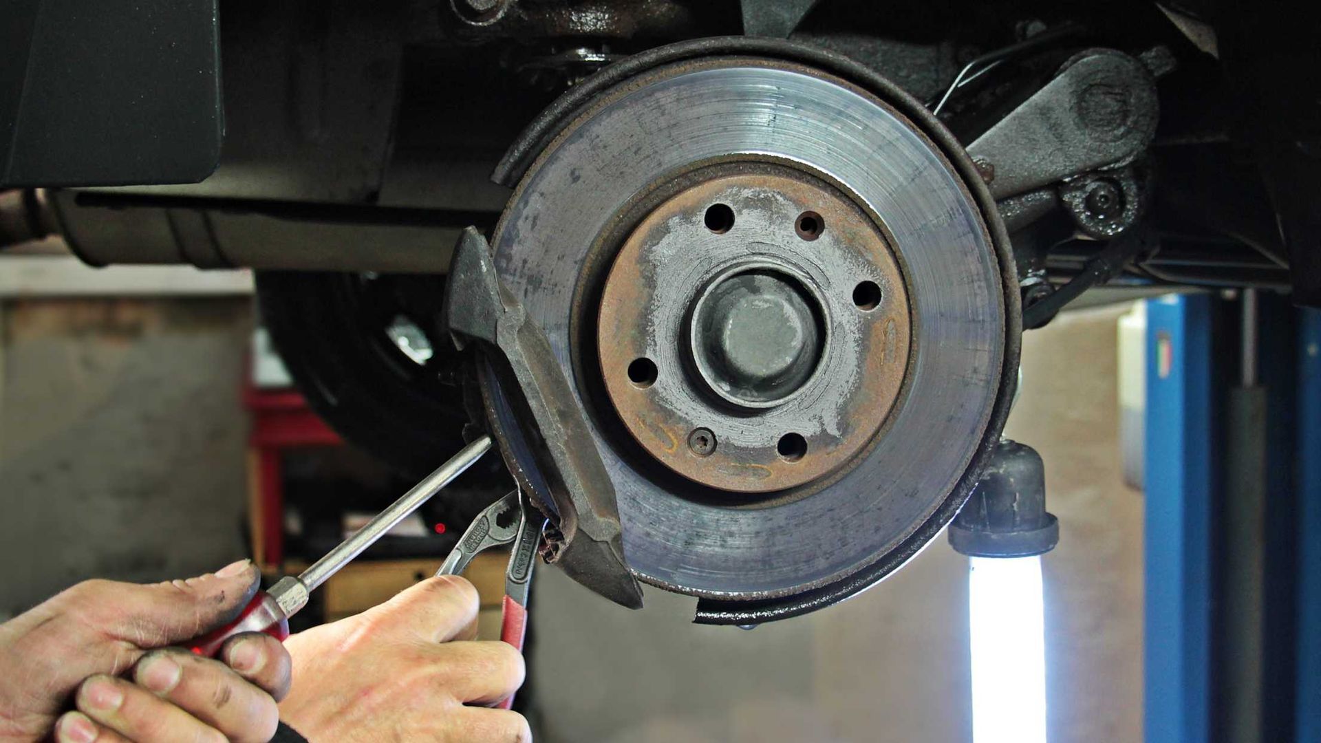 A person is fixing a brake disc on a car with a screwdriver.