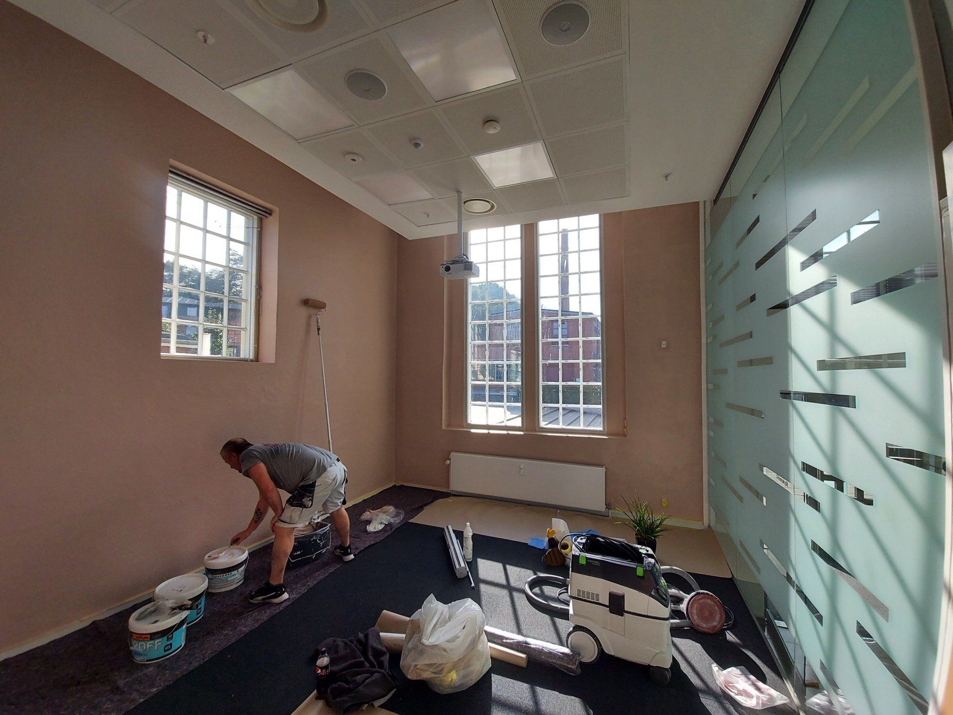 En mand maler en væg i et værelse med en støvsuger.