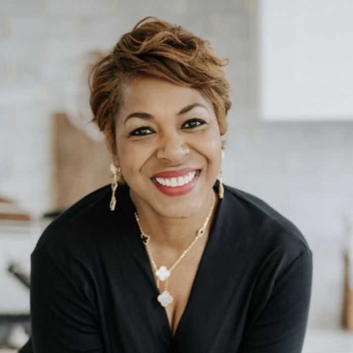 A woman wearing a black shirt and a gold necklace smiles for the camera