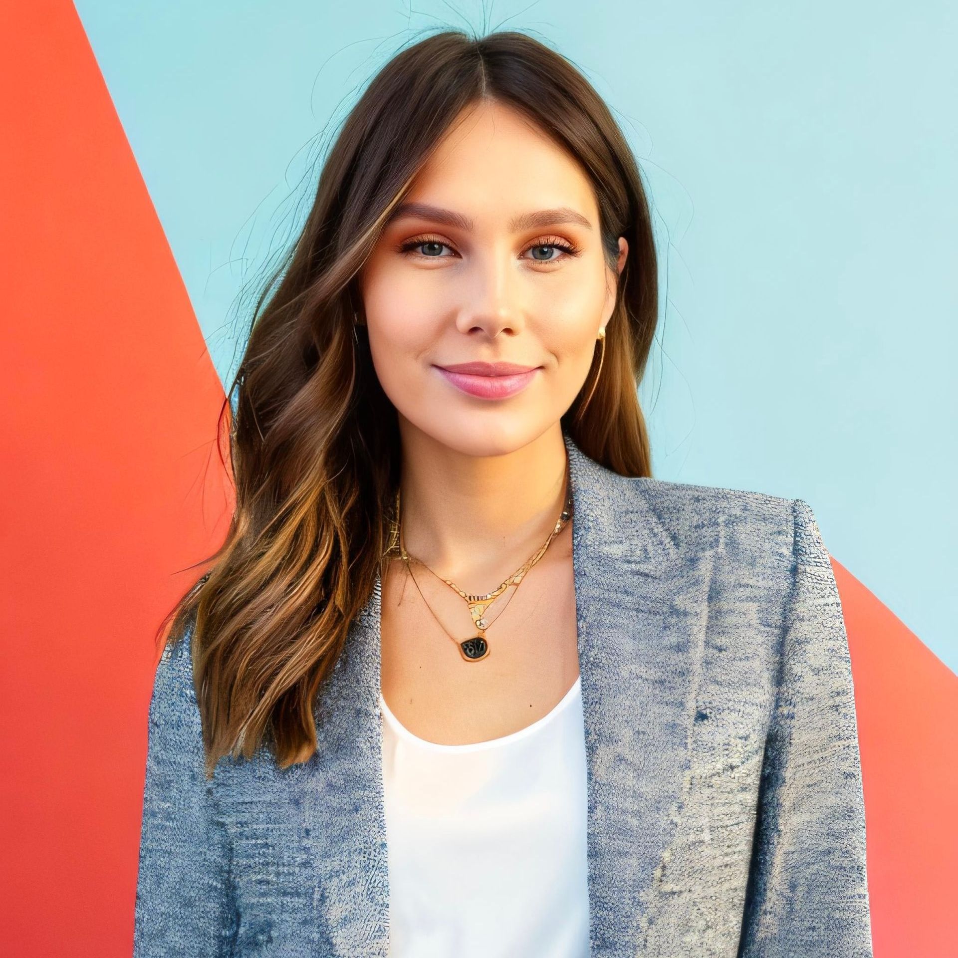 A woman wearing a gray jacket and a necklace is standing in front of a colorful wall.