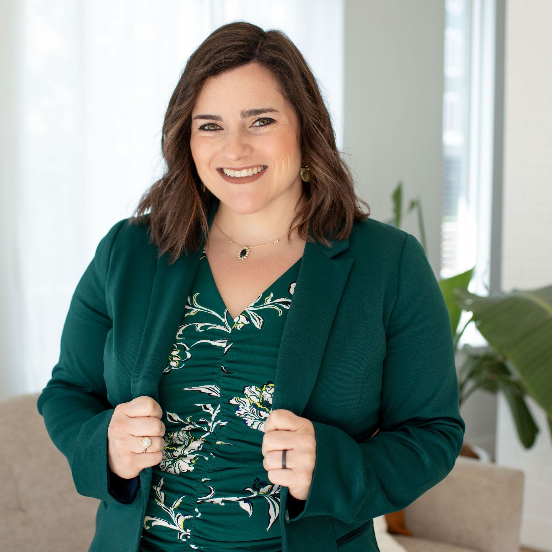 A woman in a green jacket and floral dress is smiling for the camera.