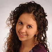 A woman with curly hair is smiling and wearing a purple shirt.