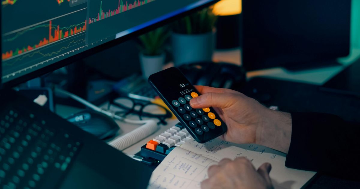 Person using a calculator, looking at a stock chart on a computer screen.