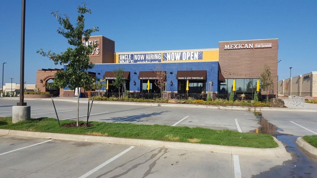 Restaurant exterior with blue and brown walls, parking lot in front, and a clear blue sky.