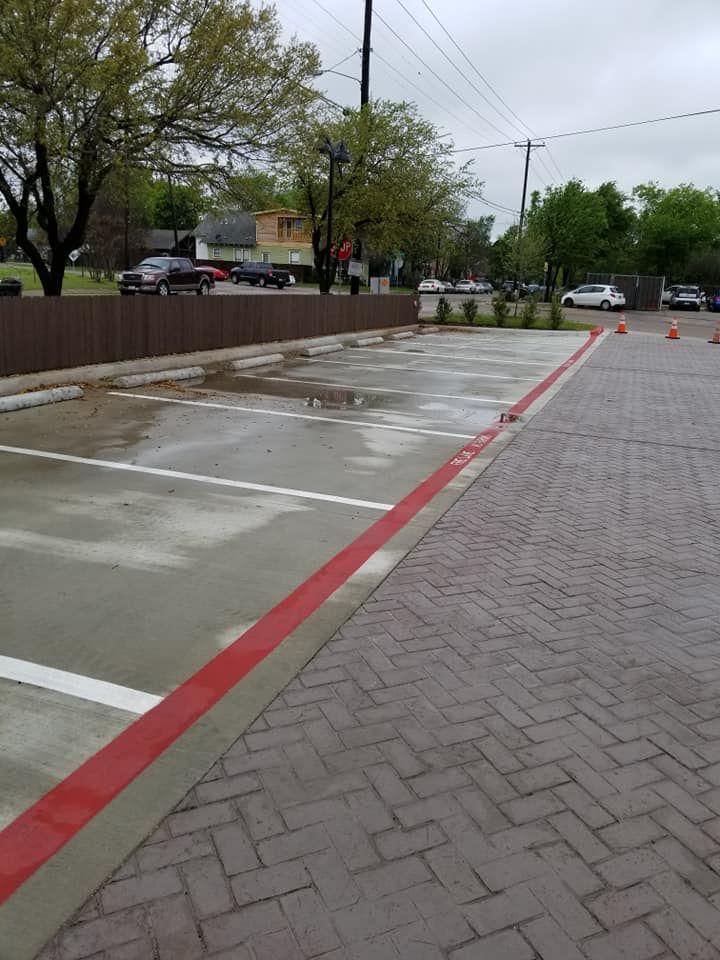 Empty parking lot with brick-like paving, wet pavement, and red curb markings under overcast skies.