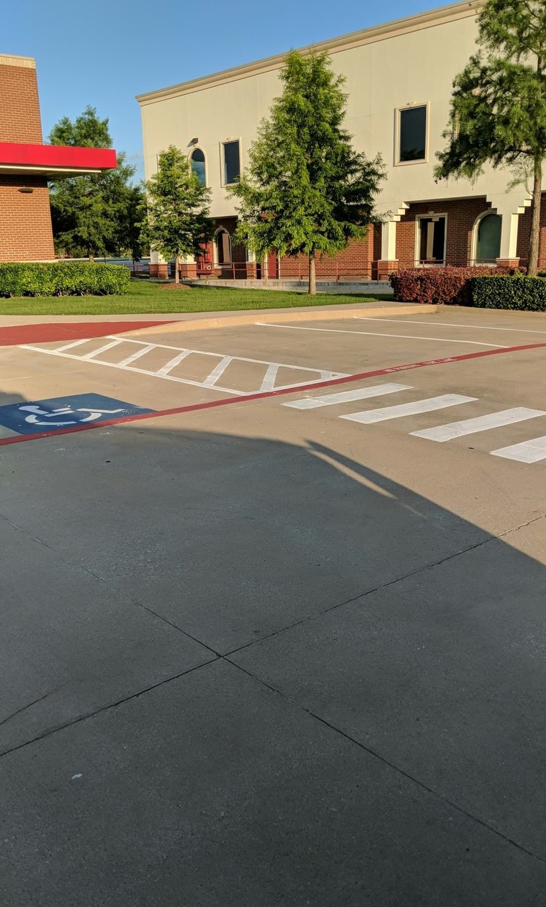 Sidewalk crossing with a crosswalk and accessible parking spaces in front of a light-colored building.