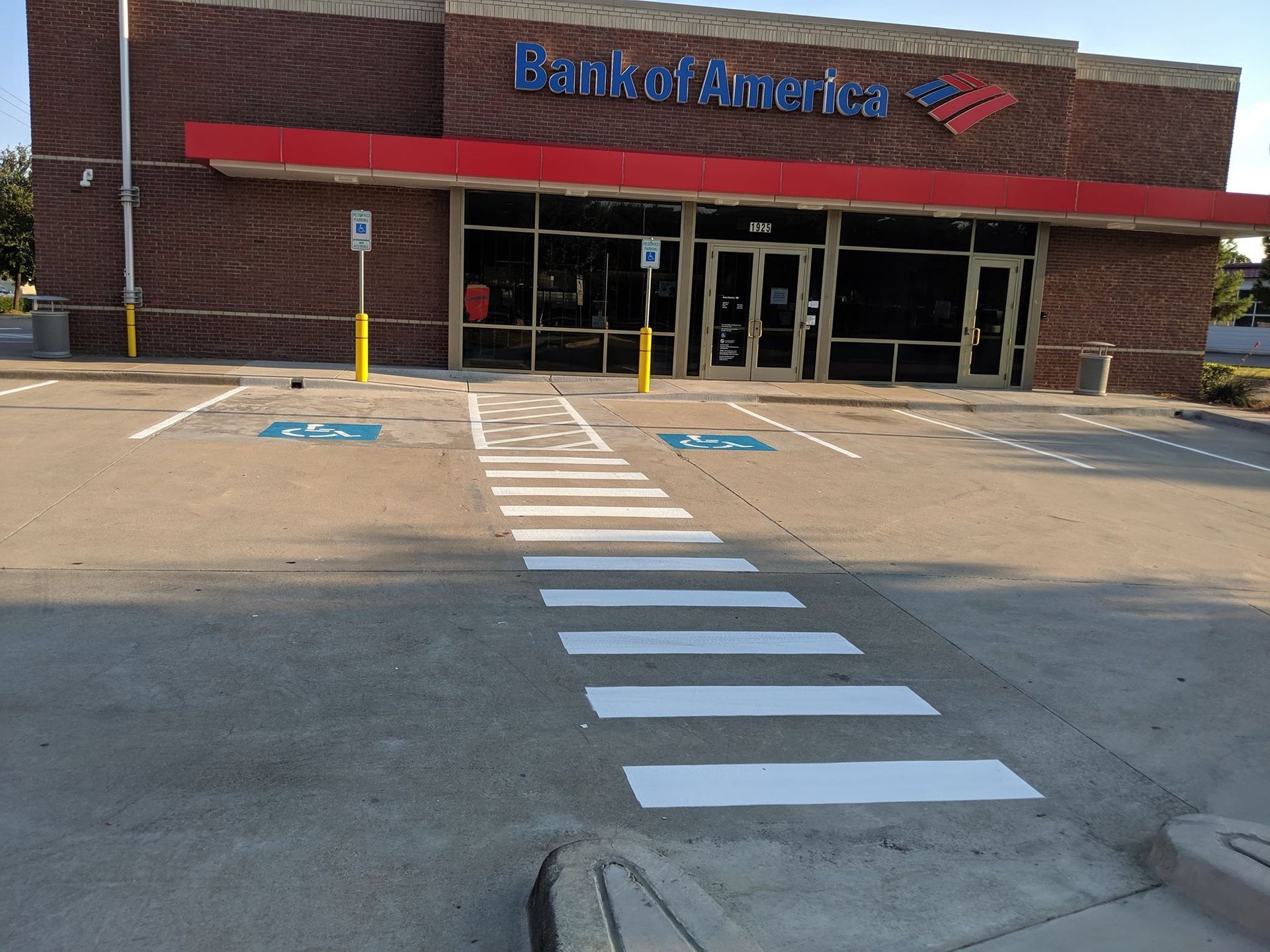 Exterior of Bank of America branch with crosswalk leading to the entrance, brick building, and red awning.