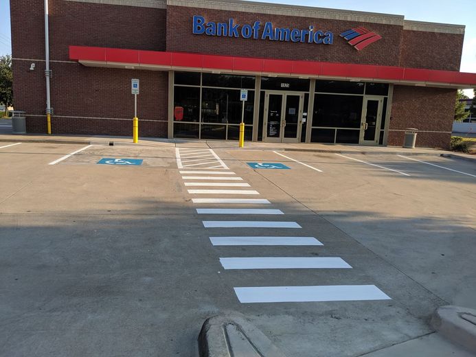 Bank of America building with crosswalk in front. Handicapped parking spaces marked. Red awning, brick exterior.