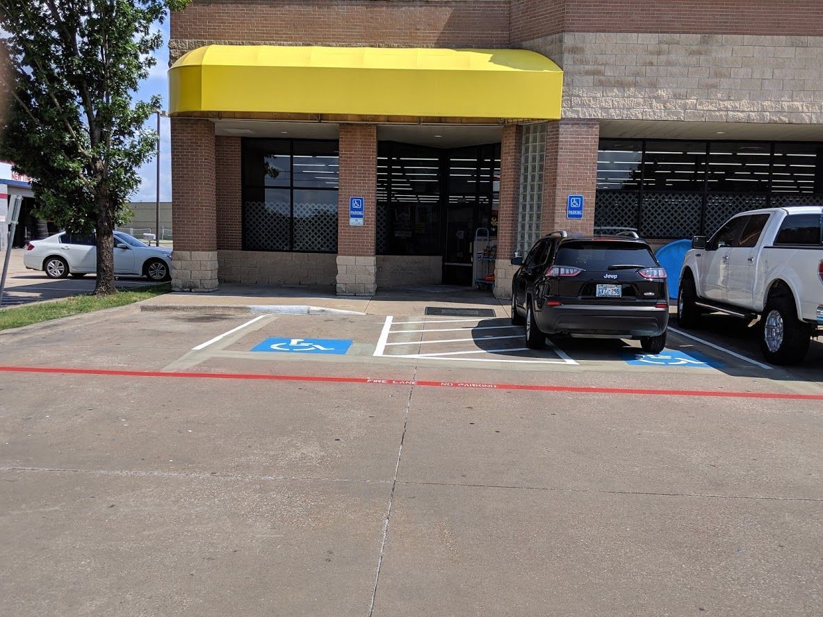 Exterior view of a building with a yellow awning and accessible parking spaces marked with blue paint.