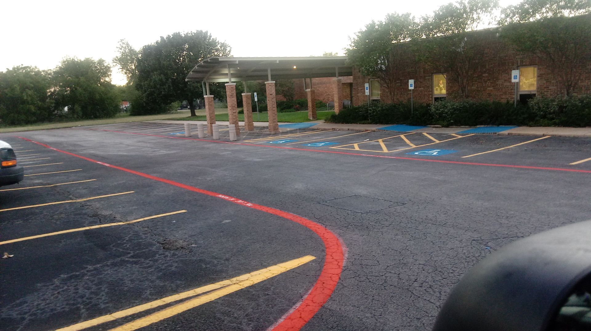 Empty parking lot with accessible parking spots near a brick building with a covered walkway.